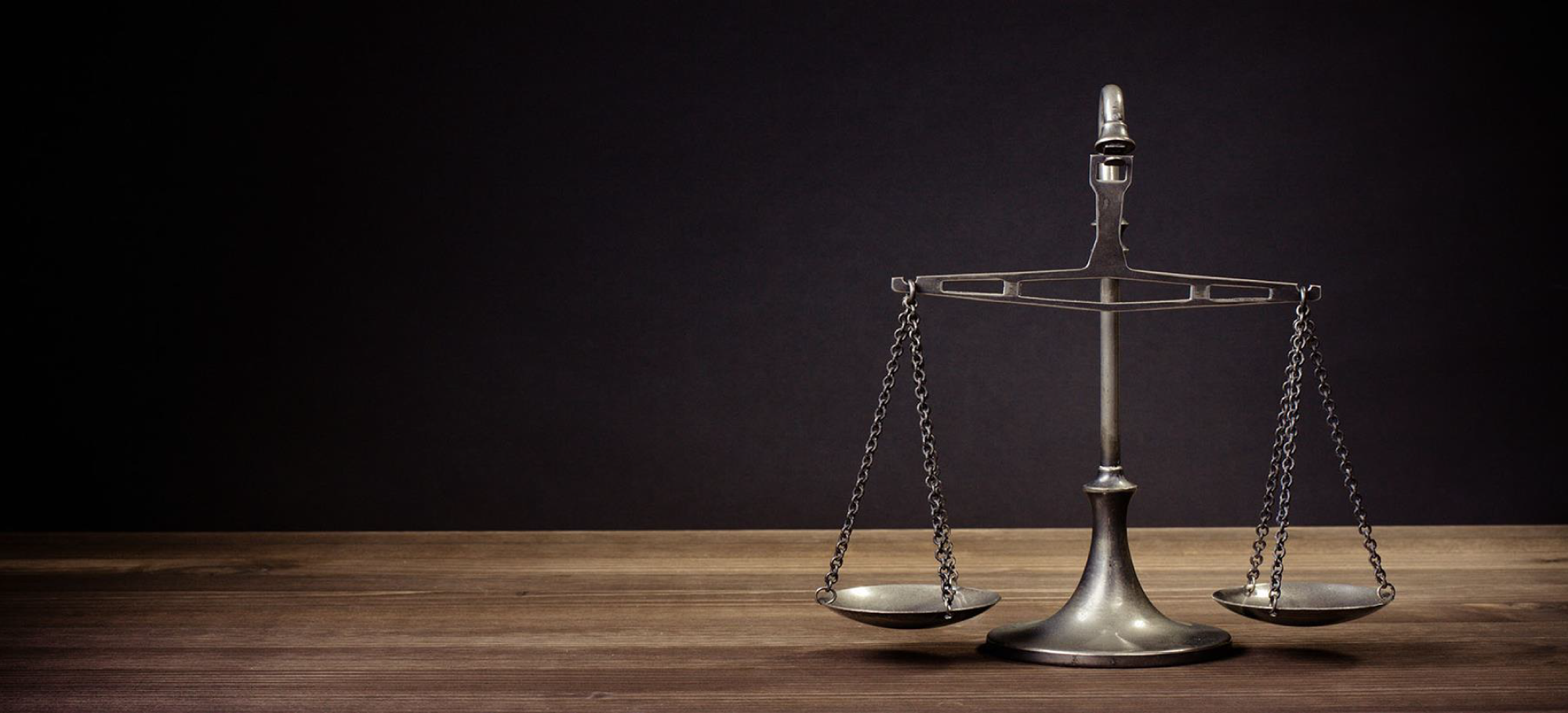 Silver justice scale on a wooden table with a dark background.